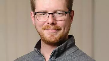 Roan Batten-Powell has short fair hair. He is wearing rectangular glasses and a grey zip-up jumper